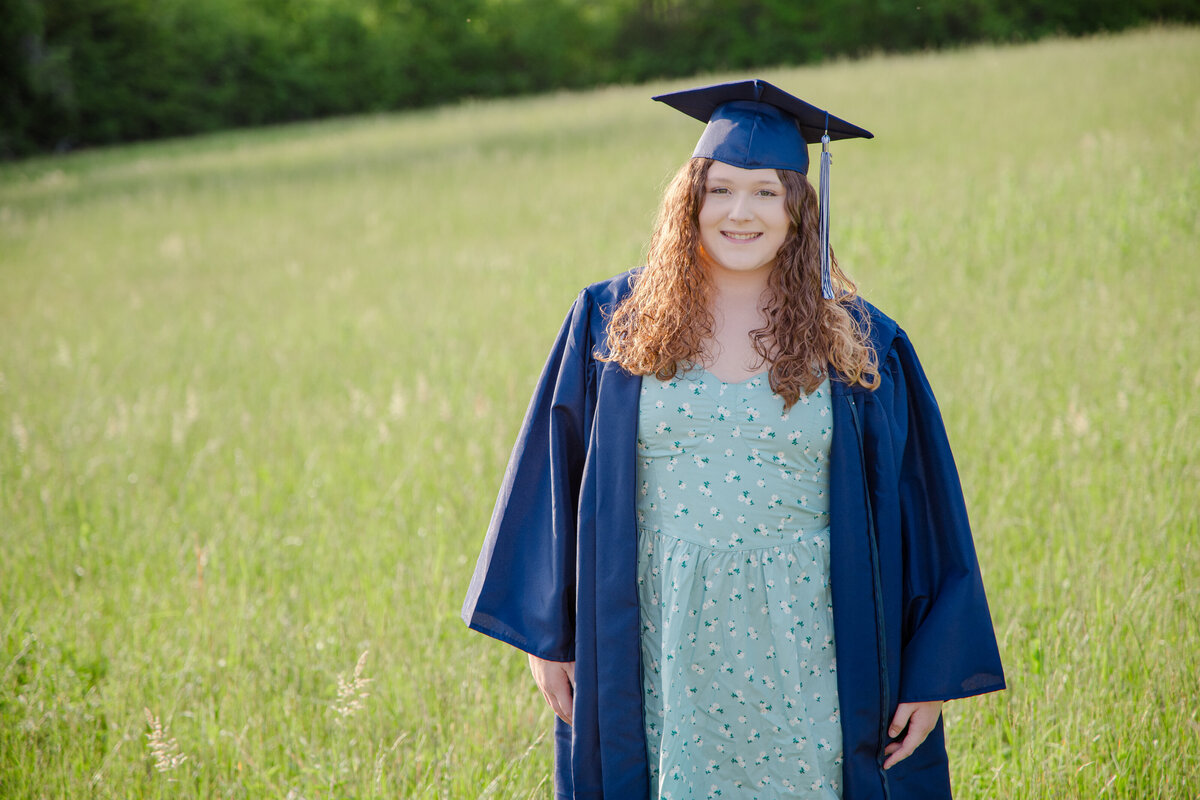 Senior girl in dress with cap and gown standing in a hay field