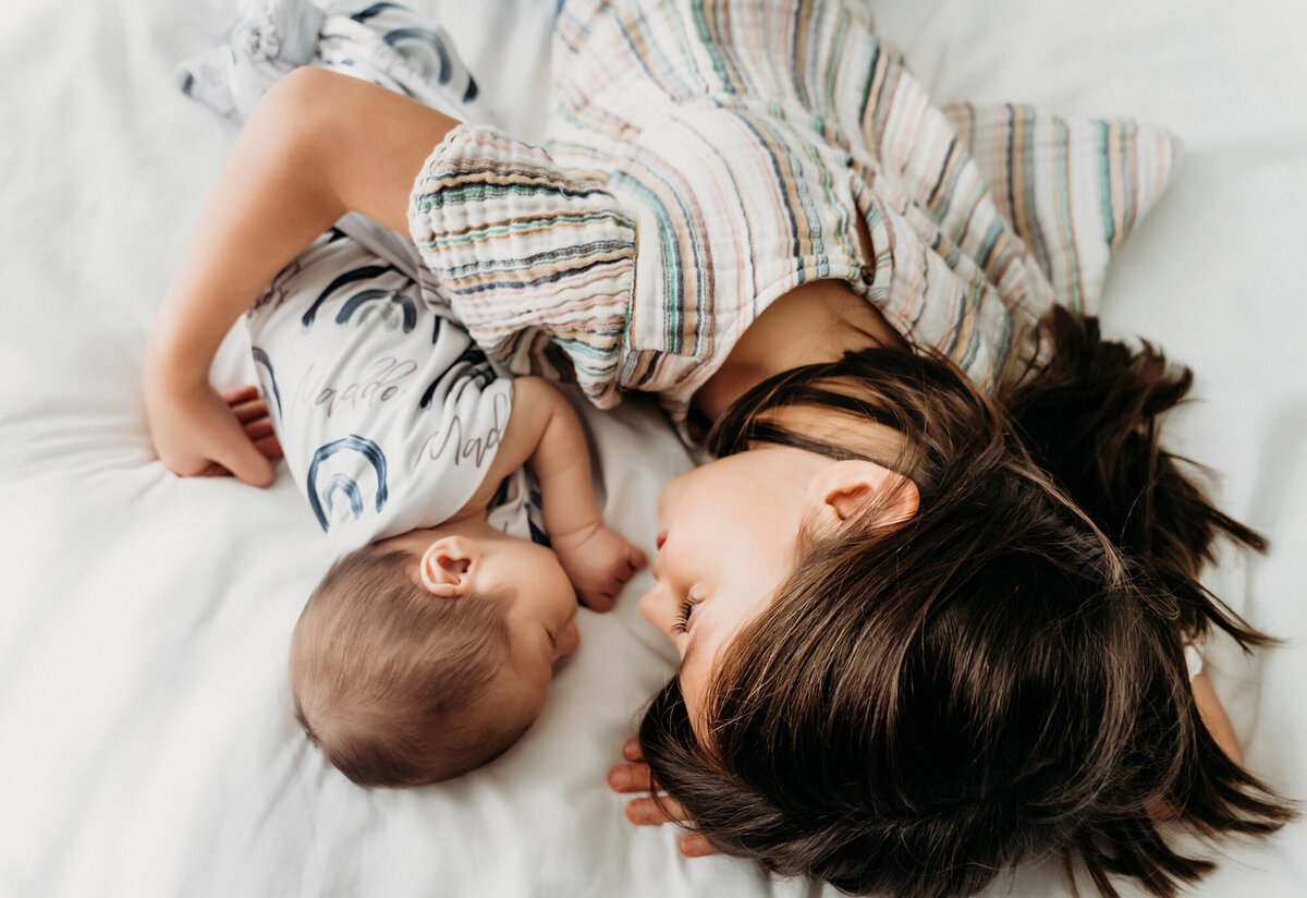 Newborn Photography, Mom holding baby girl as she gives her a kiss. Mom laying down with baby boy and snuggling him.