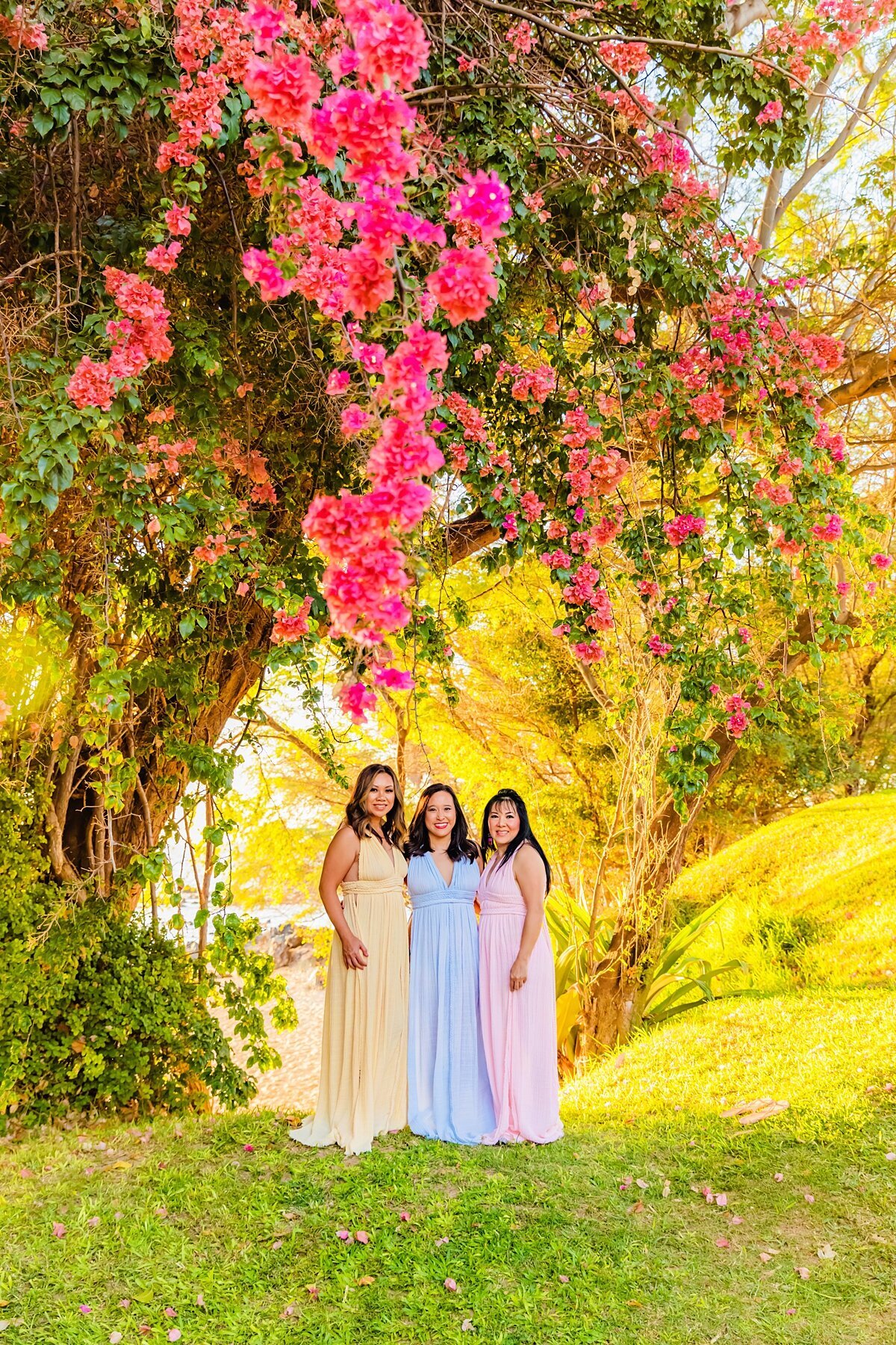 Three women wearing Kasia Kulenty Selena gowns pose below pink bougainvillea tree in Wailea