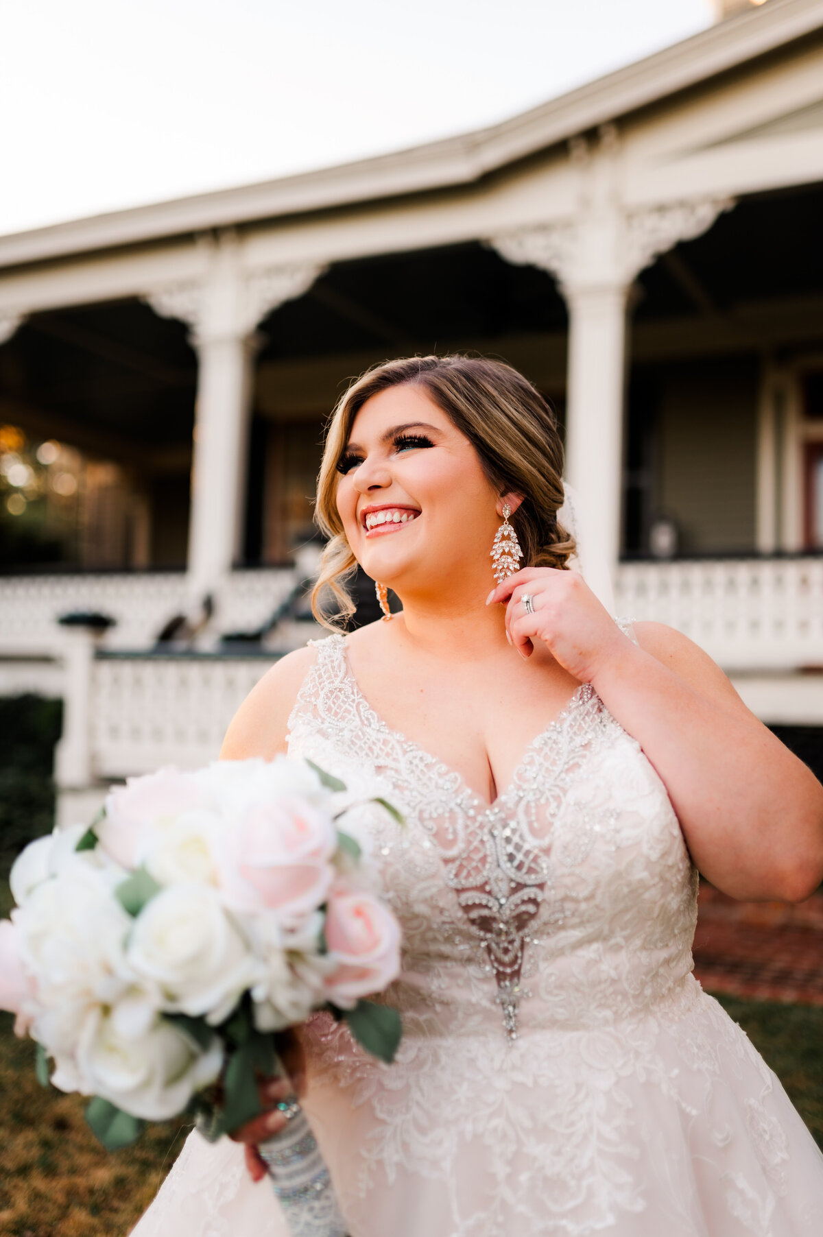 luxury wedding bridals with bride in a lace wedding gown holding a finger up to her earring and smiling to the distance