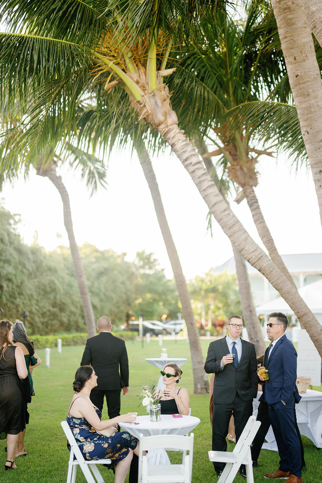 Wedding guests mingle under swaying palm trees during Stephanie and Bradley’s tropical cocktail hour at The Islander Resort in Islamorada. Captured by Claudia Amalia Photography.