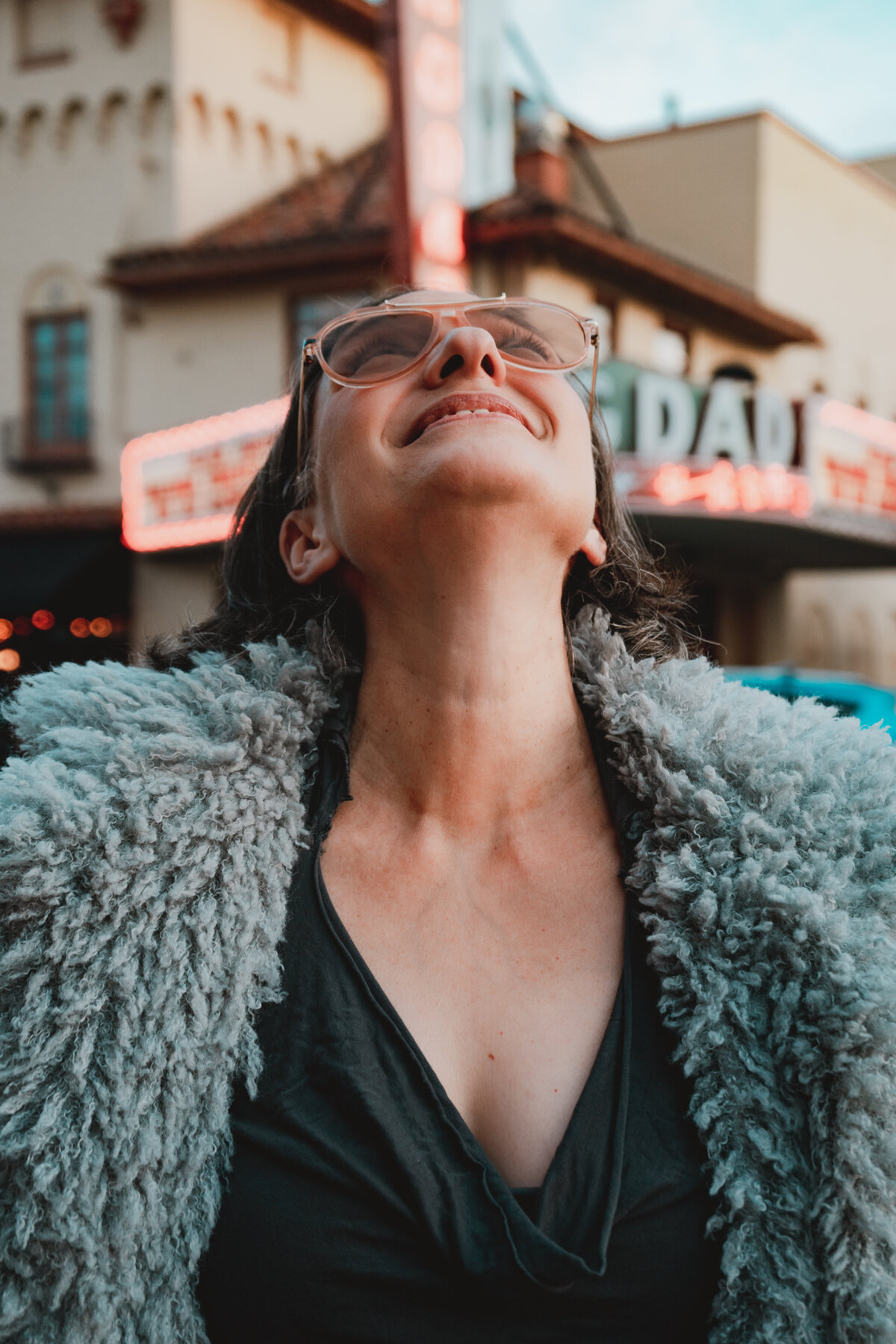 Woman in grey faux fur smiling in front of a red theater sign – joyful brand image for creatives by Mewphotovideo