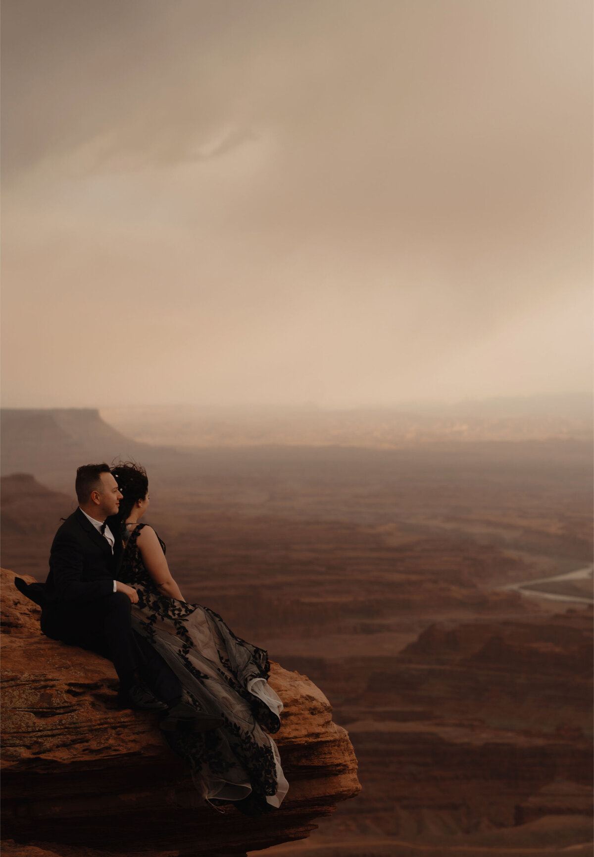 Moab, Utah elopement couple sits together on a rock and looks out at the scenery of Dead Horse Point State Park