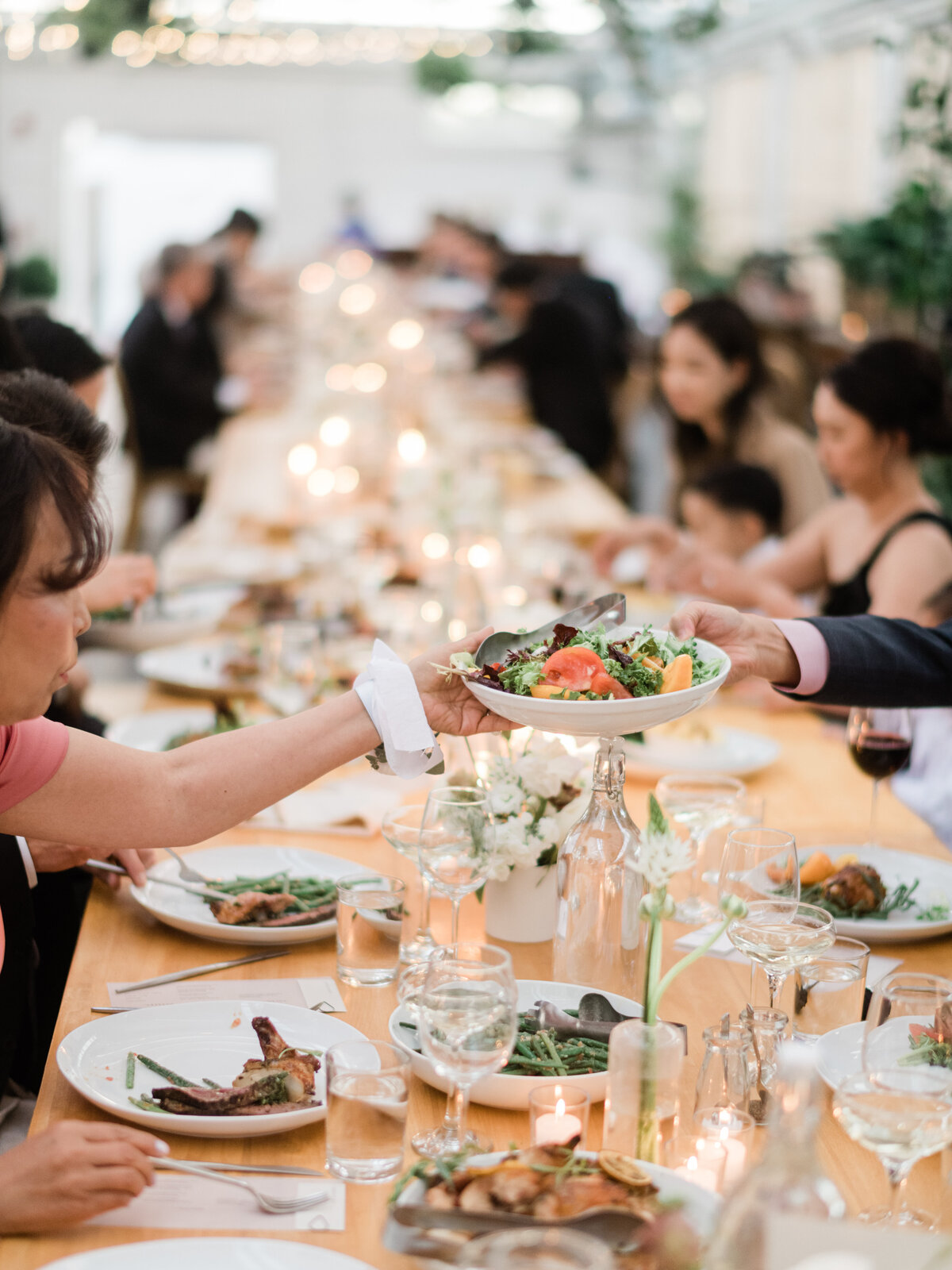 Long table filled with guests passing shared plates at an intimate company dinner at Audrey’s Farmhouse.