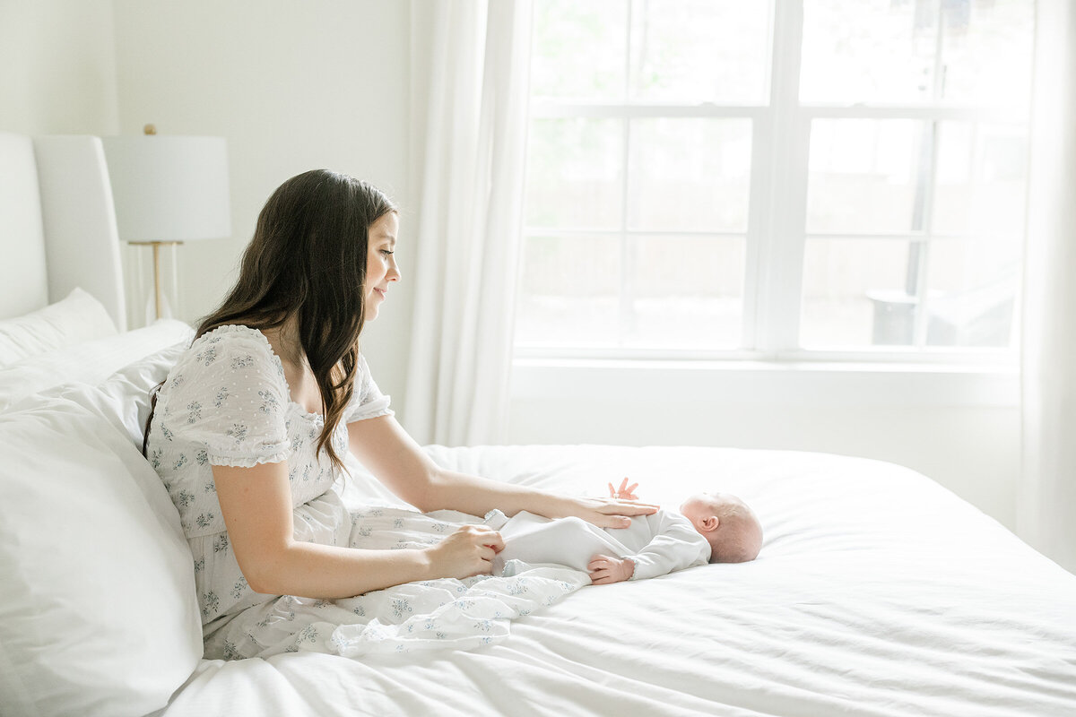 a mother hanging out with her newborn on a white bed