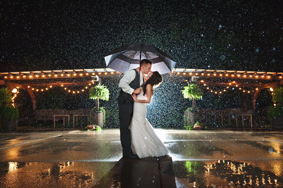 Wedding couple with umbrella kissing in the rain.