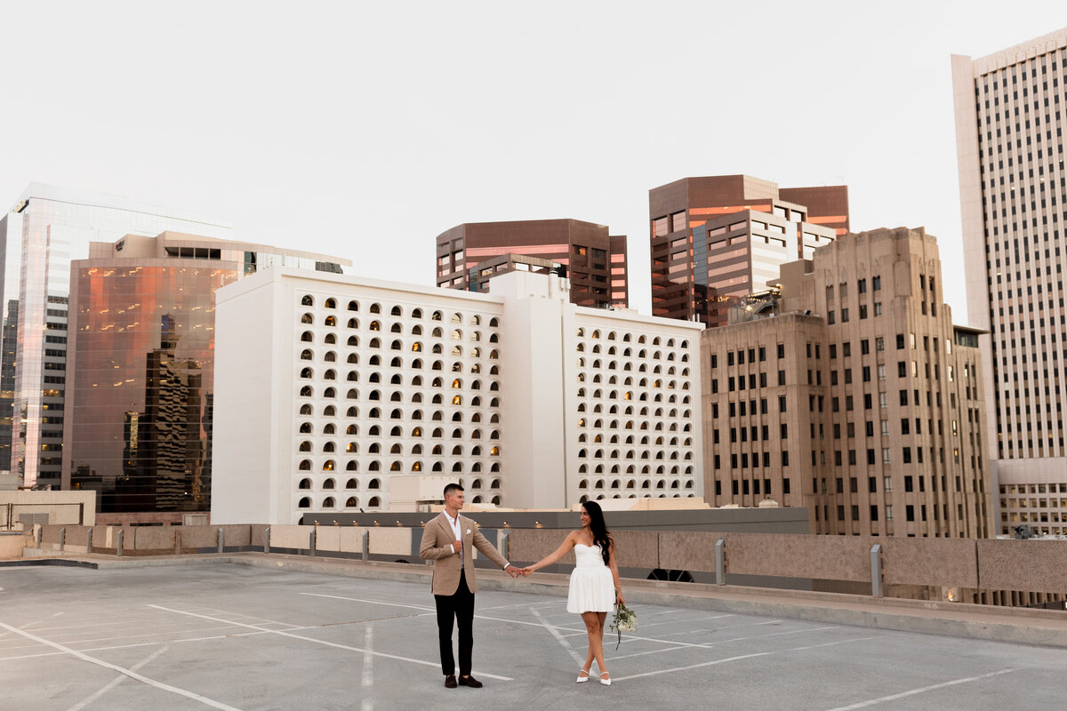 man and a woman standing at the top of a gragae rooftop in downtown phoenix arizona holding hands and looking at eachother