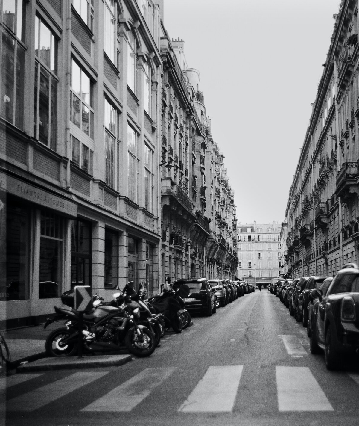 black and white image of cars parked on a street in europe