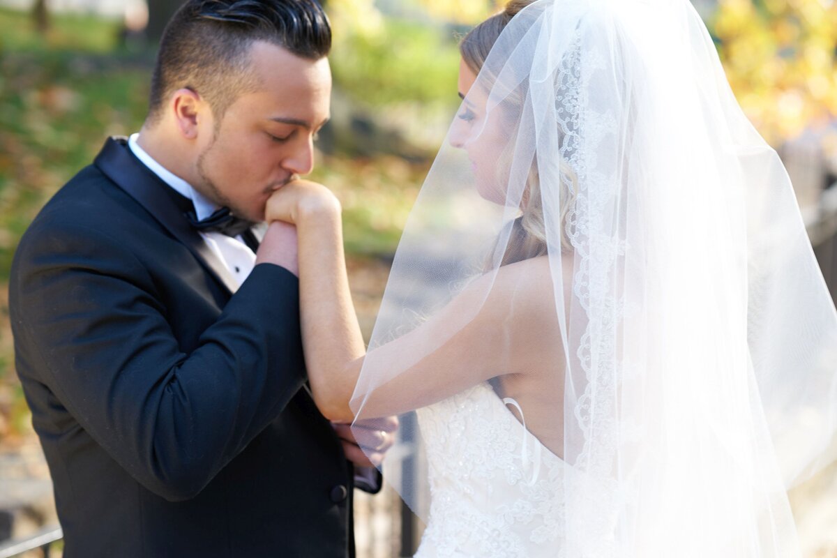 The groom delicately kisses the bride's hand, symbolizing his love and devotion. This romantic gesture highlights their affection and adds a classic touch to their wedding day photos.