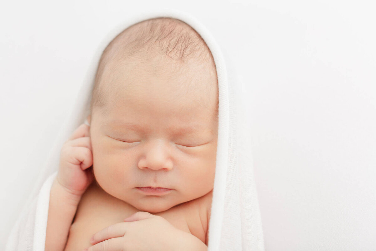 Newborn baby sleeping on white blanket during newborn photoshoot.