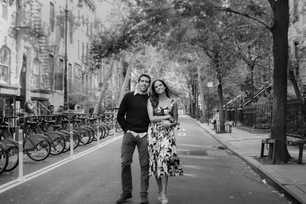 Black and white photo of the engaged couple in a street beside a bike station in West Village, NYC. Image by Jenny Fu Studio.