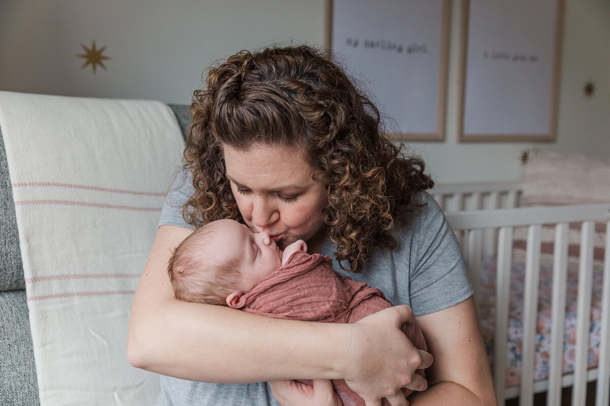 Mom Kisses Newborn in Home Nursery