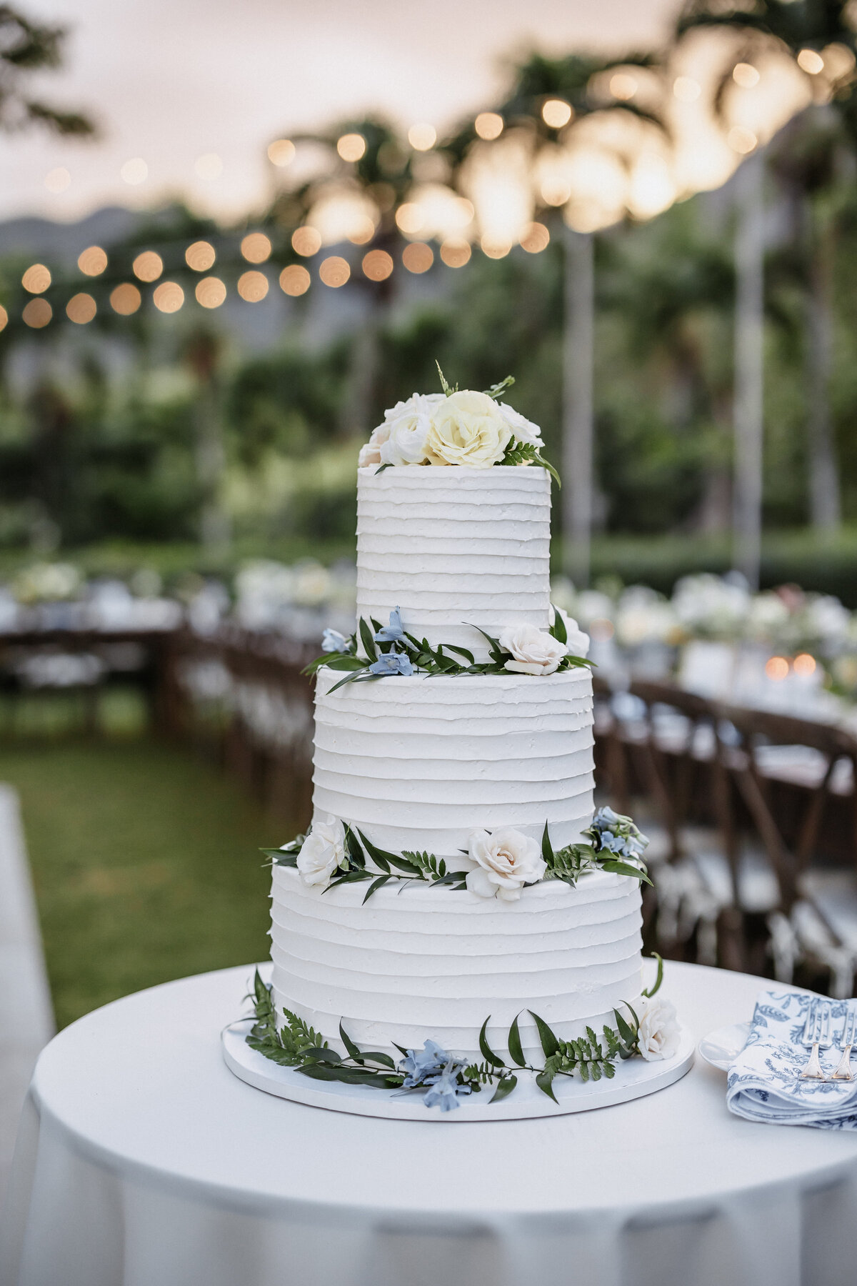 Three tier wedding cake with blue and white florals, and greenery
