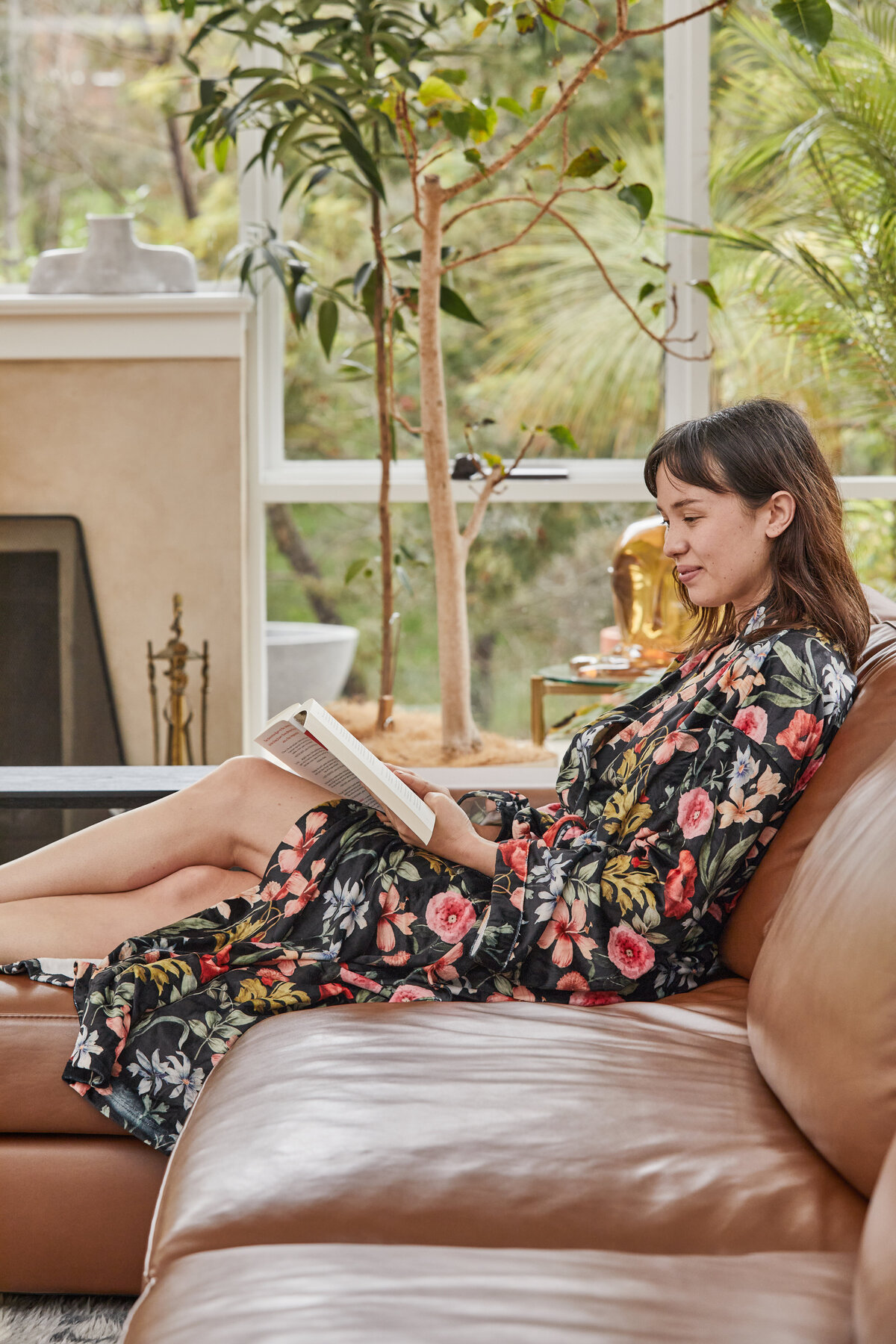 Woman reading on leather sofa in light-filled living room styled with greenery by interior designer Melbourne