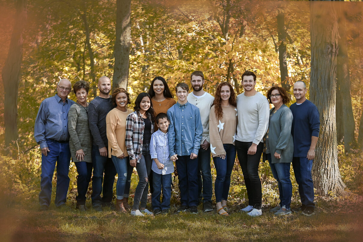 Family stands side by side in the woods with fall trees