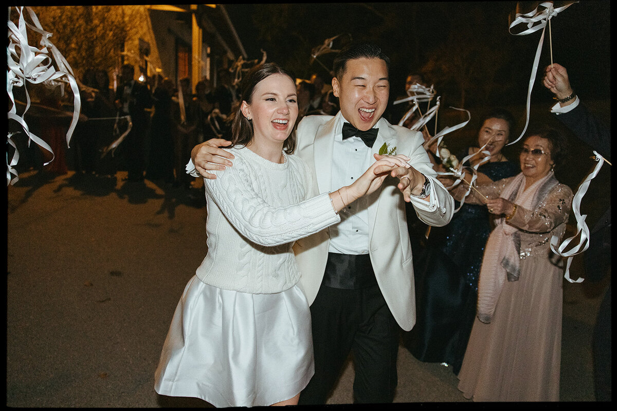 Bride and groom dash through their sendoff streamers as they exit reception in New York style wedding. 