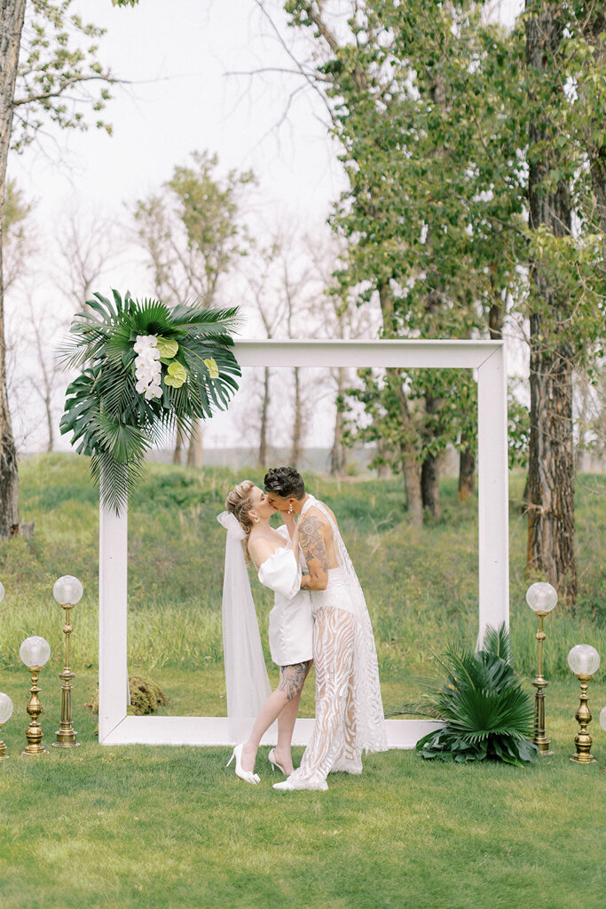 Couple kissing during wedding ceremony at Sugar Pine Island, a romantic wedding venue in Foothills, Alberta, featured on the Brontë Bride Vendor Guide.