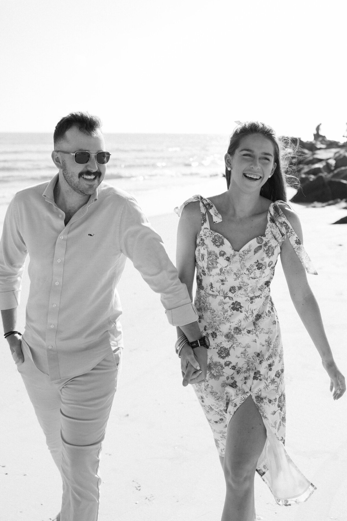 Smiling couple hold each others hands walking down the shore at the beach