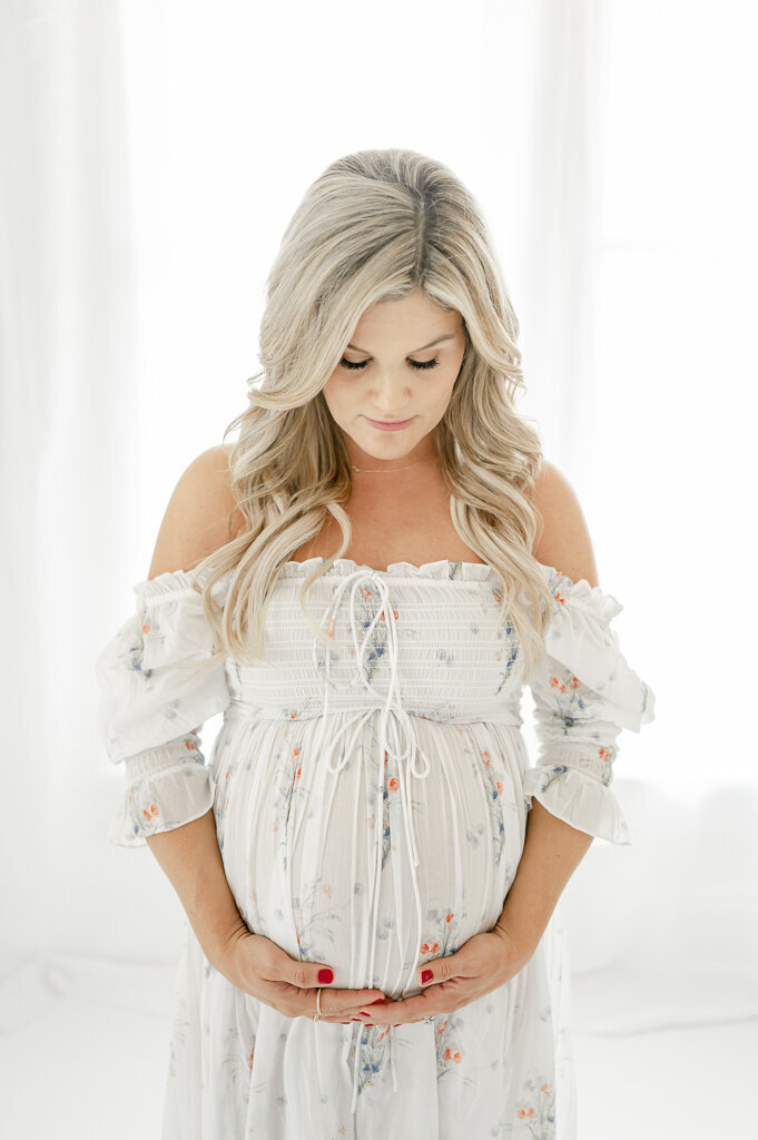 Pregnant woman holds her belly wearing a Doen floral bouquet dress By Nashville maternity photographer Kristie Lloyd