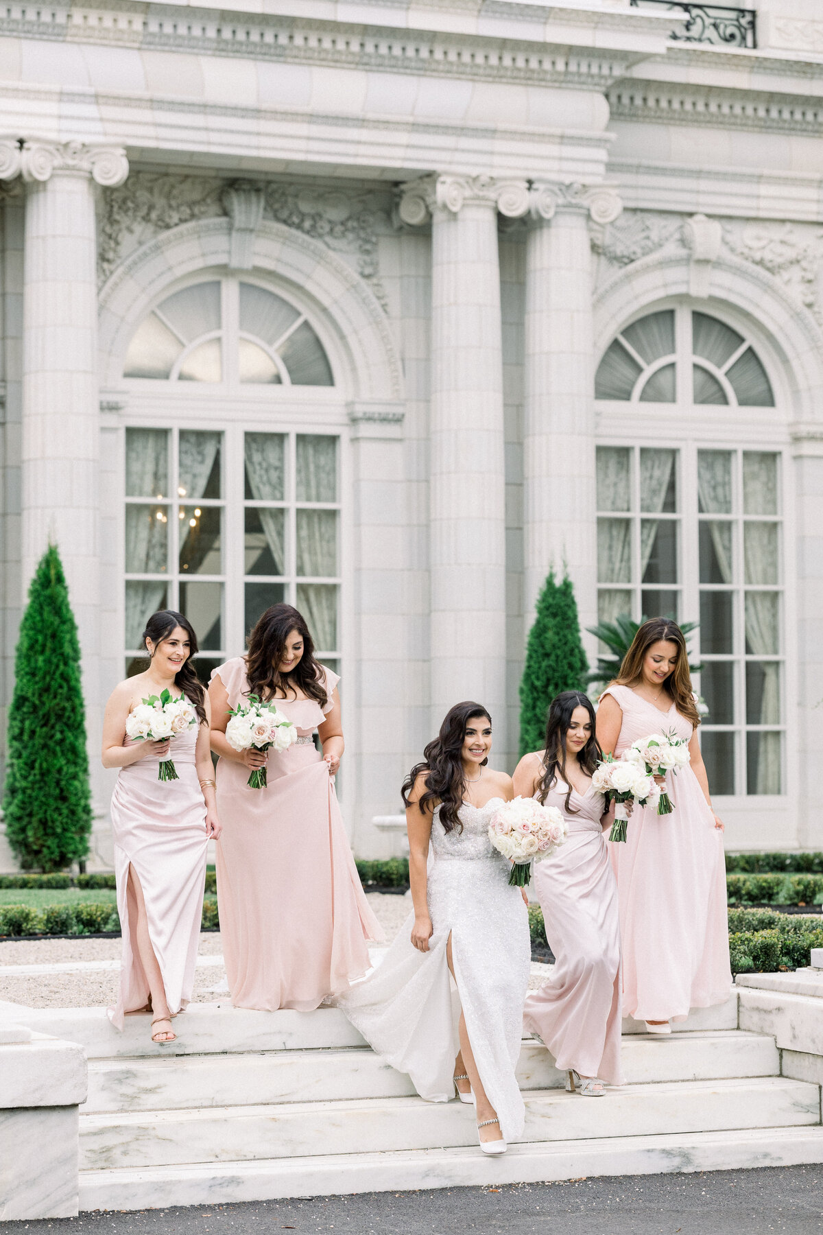 bridesmaids walk down the stairs for candid portraits in front of rosecliff mansion