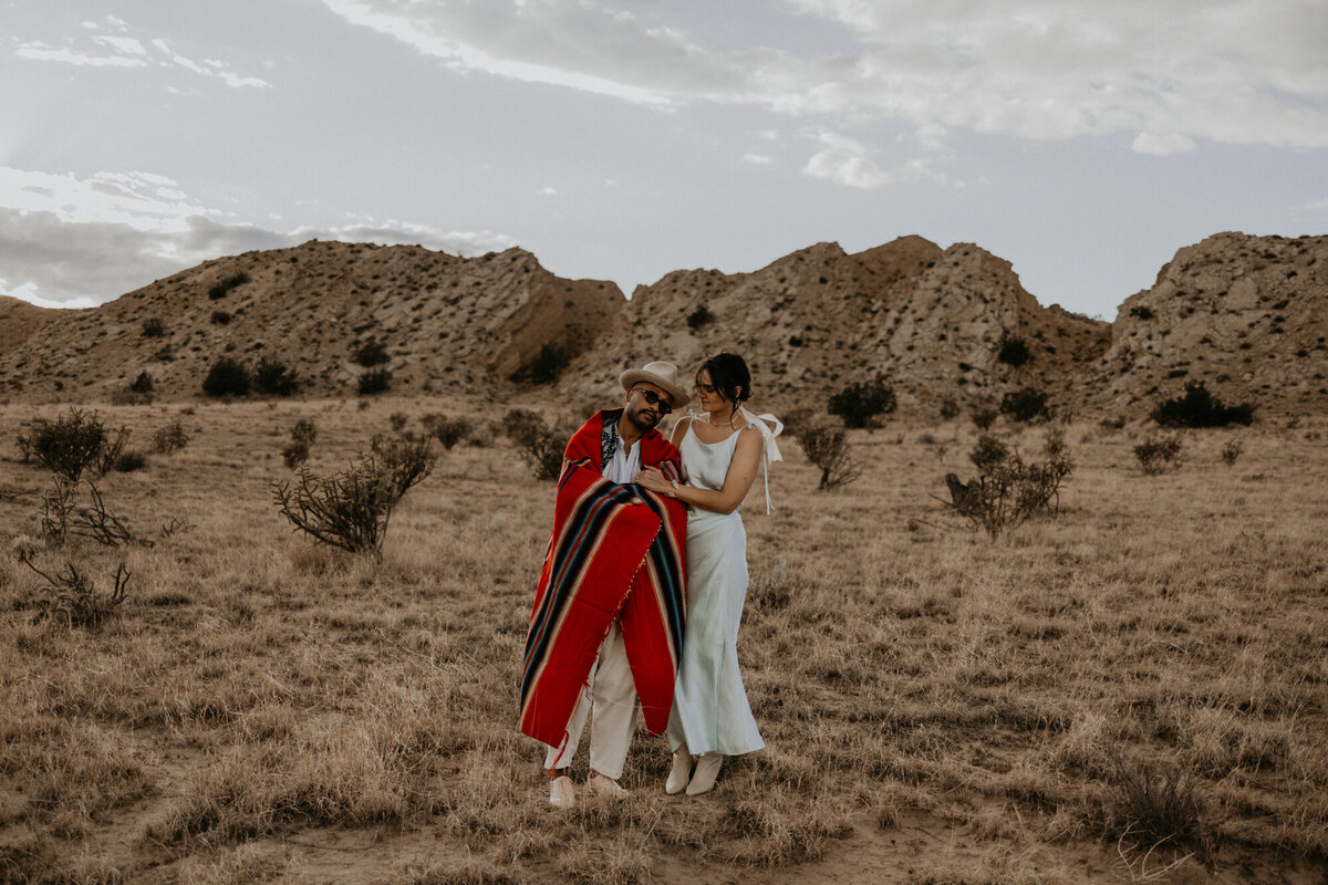 A bride and groom standing together in the desert with colorful outfits