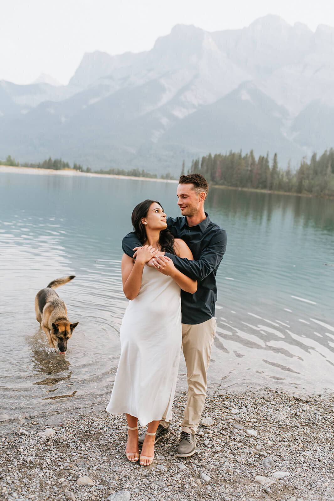 Man-hugs-woman-in-front-of-water-with-dog