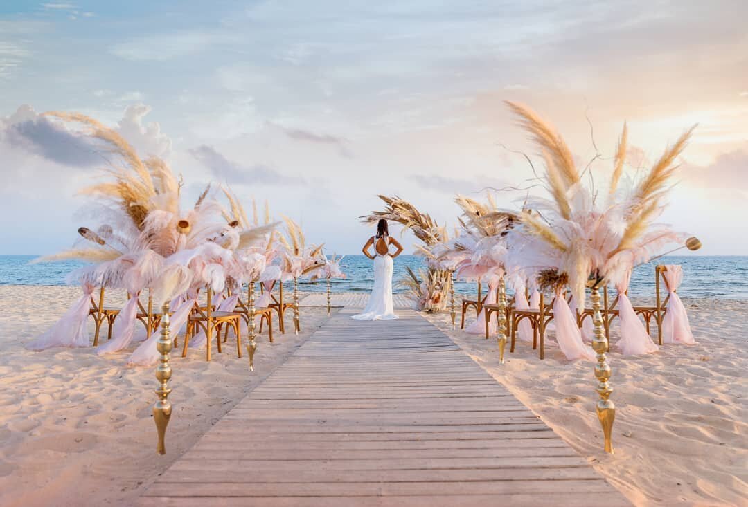 Stunning tall decor lines the aisle with rustic grasses looking towards a bride standing in the ceremony area