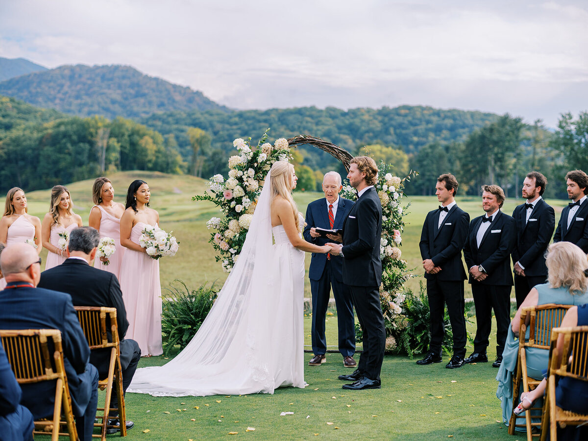 Bride and groom exchanging vows under a floral arch during an outdoor ceremony at Waynesville Inn and Golf Club with Blue Ridge Mountain views.