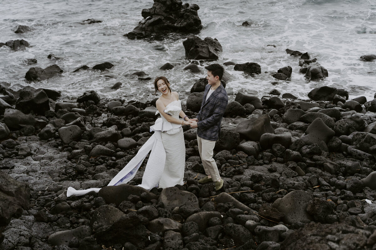 the couple holding hands and laughing while standing on the rocks of cactus coastline