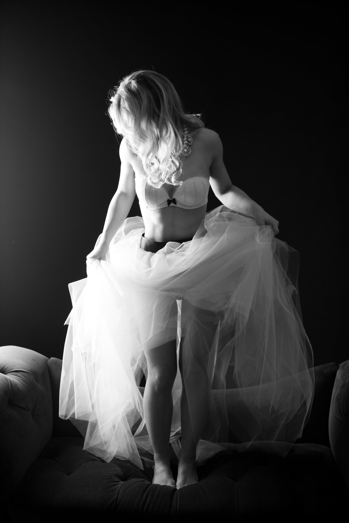 Black and white photo taken in a New York photography studio by a boudoir photographer. Woman standing on a couch in a bra and a fluffy tulle skirt.