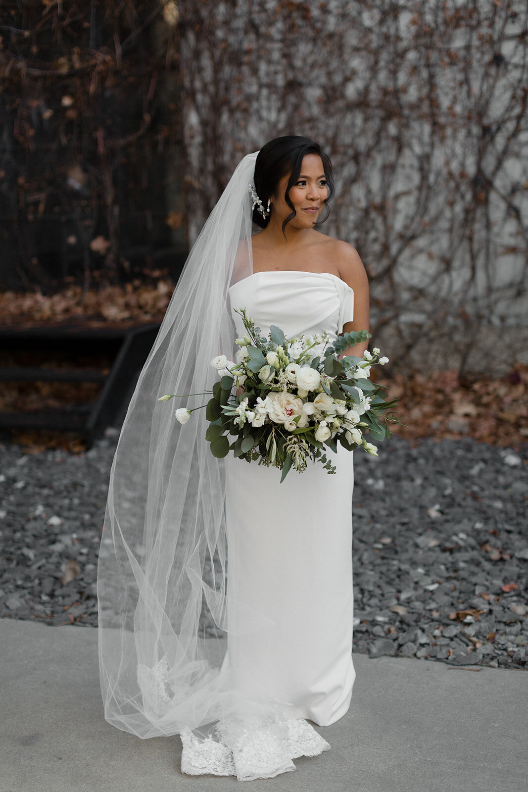 bride stands in courtyard with large white bouquet