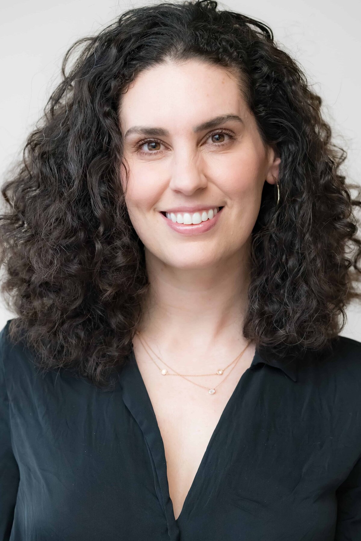Close-up headshot of a woman smiling with long, dark, curly hair