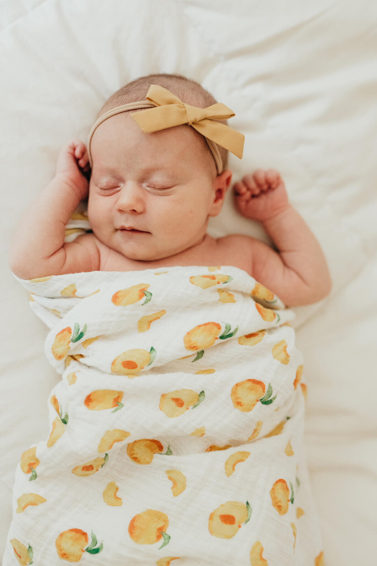 A baby girl wrapped in a peach patterned swaddle and wearing a soft golden bow sleeps peacefully during her photoshoot with Allison Wolf, Boston Newborn Photographer