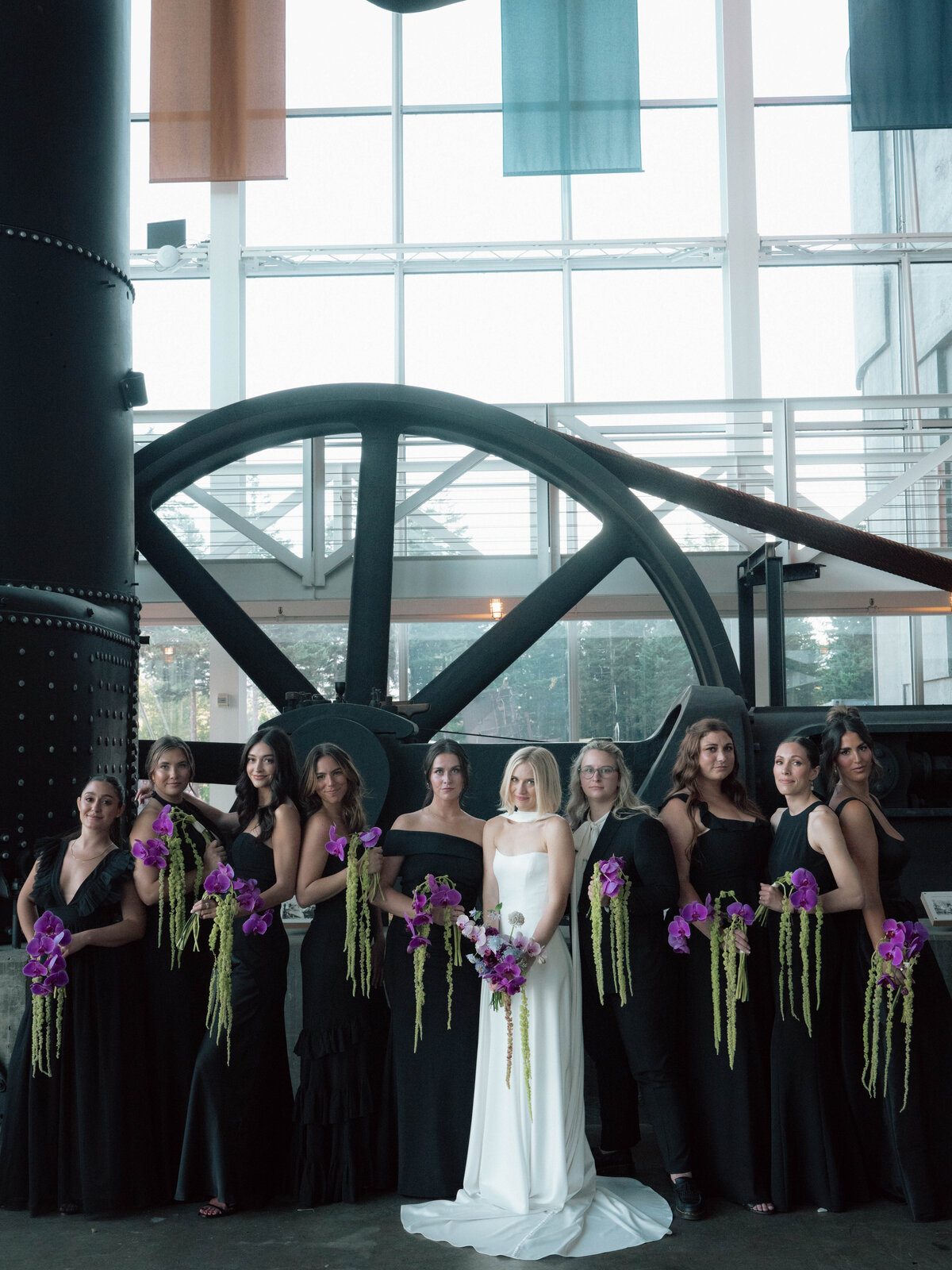 Bride with bridesmaids in black dresses holding vibrant purple bouquets