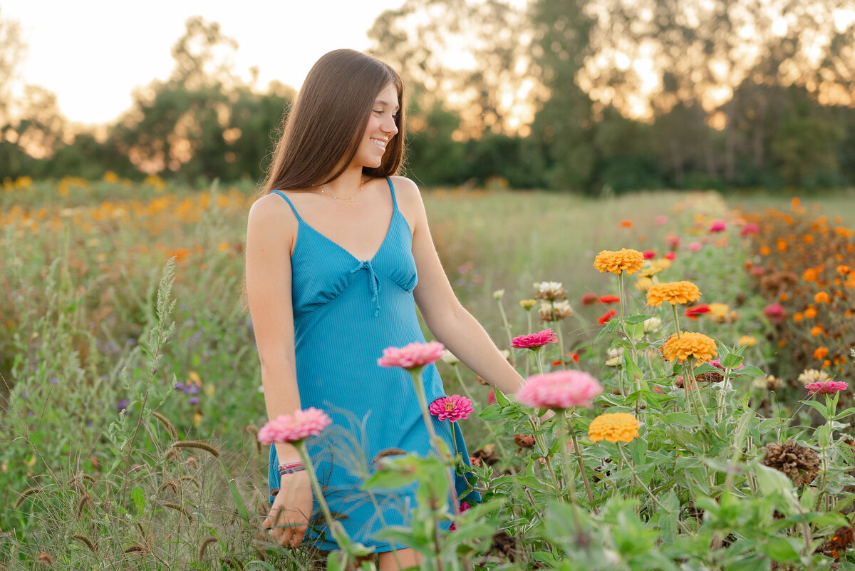 High school senior girl standing in a flower meadow, smiling softly.