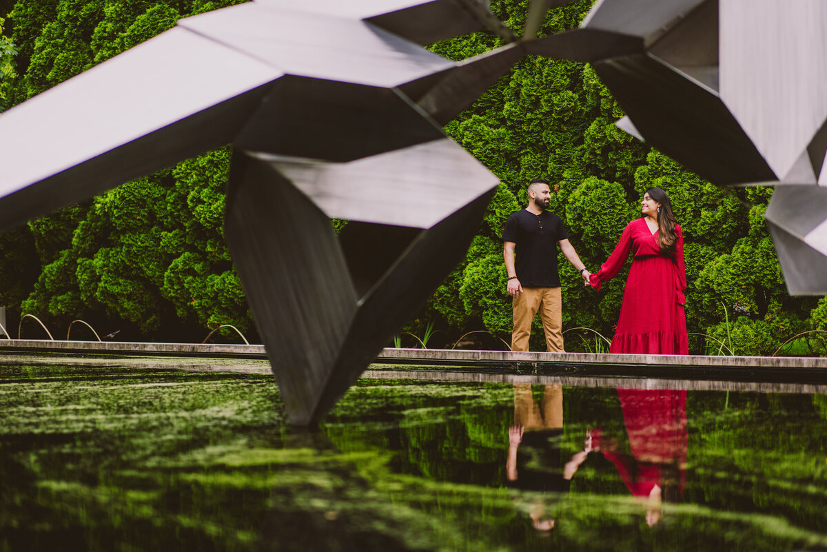 A couple standing near a metal structure with their reflection in a pool at grounds for sculpture in nj