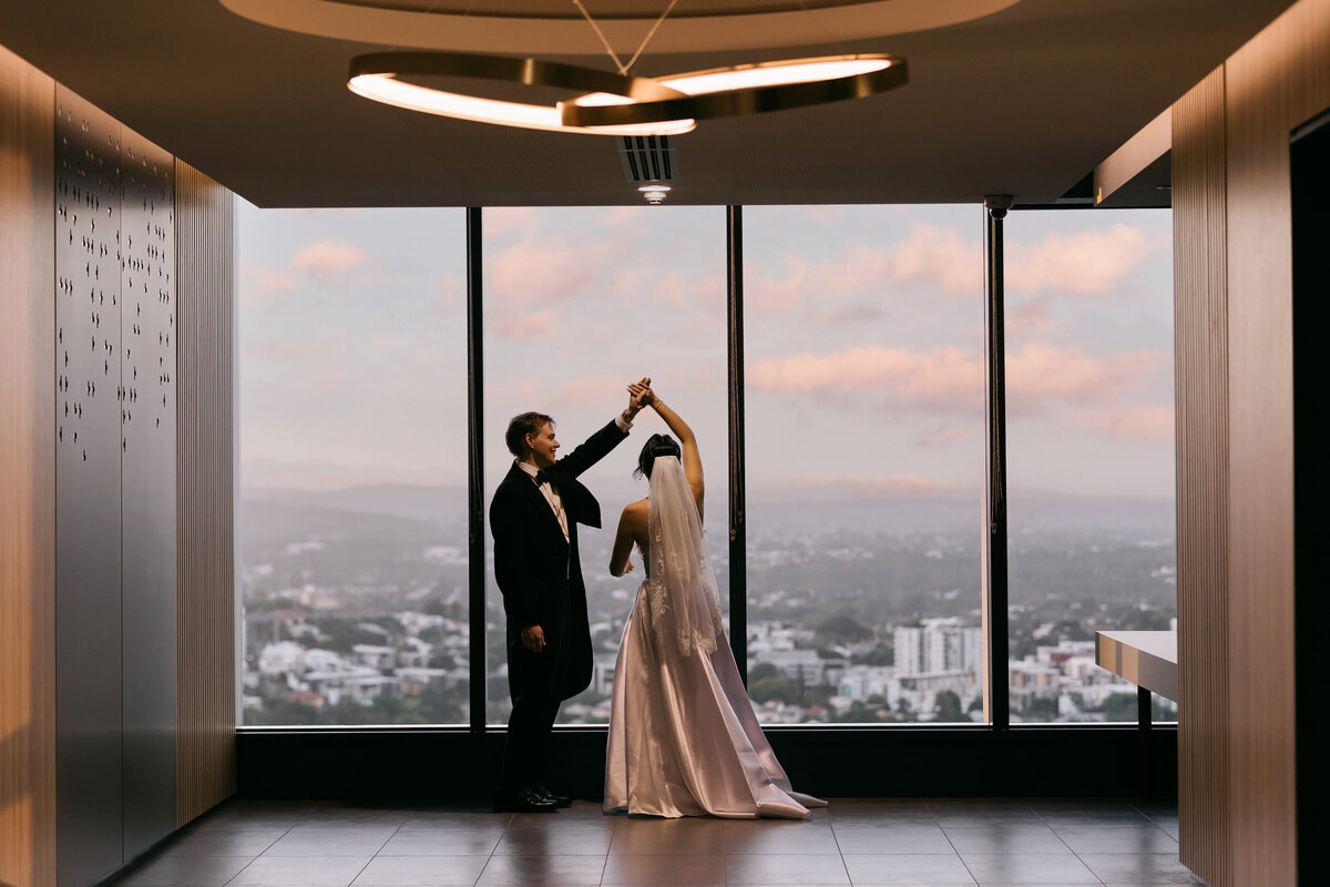 Bride and groom dancing in front of the floor-to-ceiling windows at sunset inside Brisbane Registry Office — modern and romantic registry marriage photography.