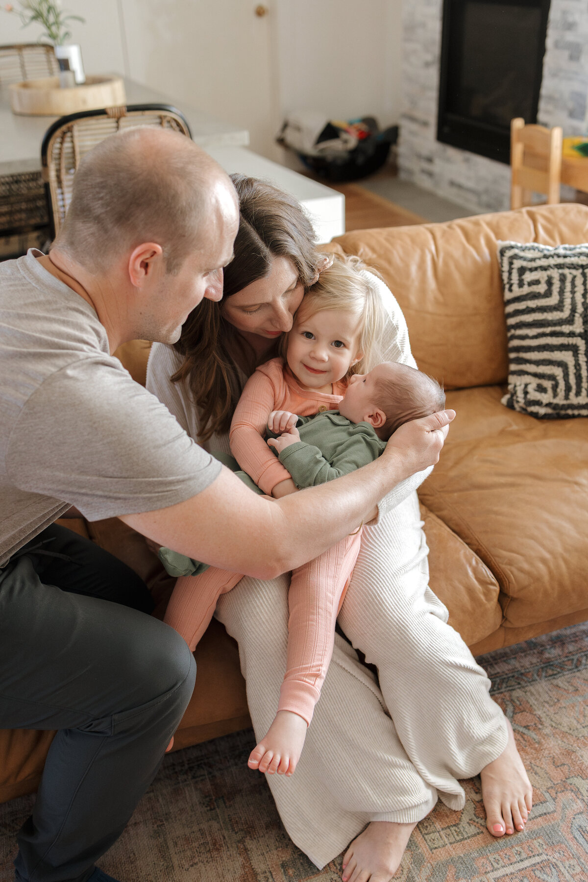Longmont dad helping toddler hold newborn baby while sitting in moms lap