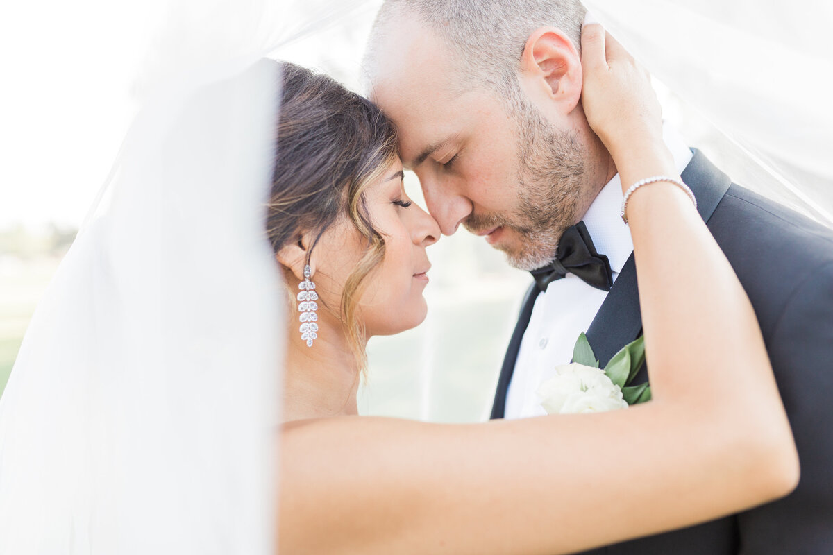 Close up shot of bride and groom nose to nose with her veil floating in the wind