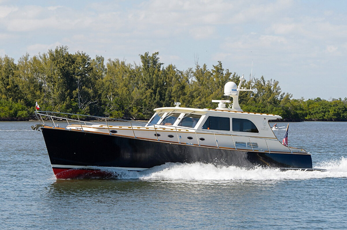 A sleek motor yacht cruises on a calm waterway, surrounded by lush green trees and vegetation