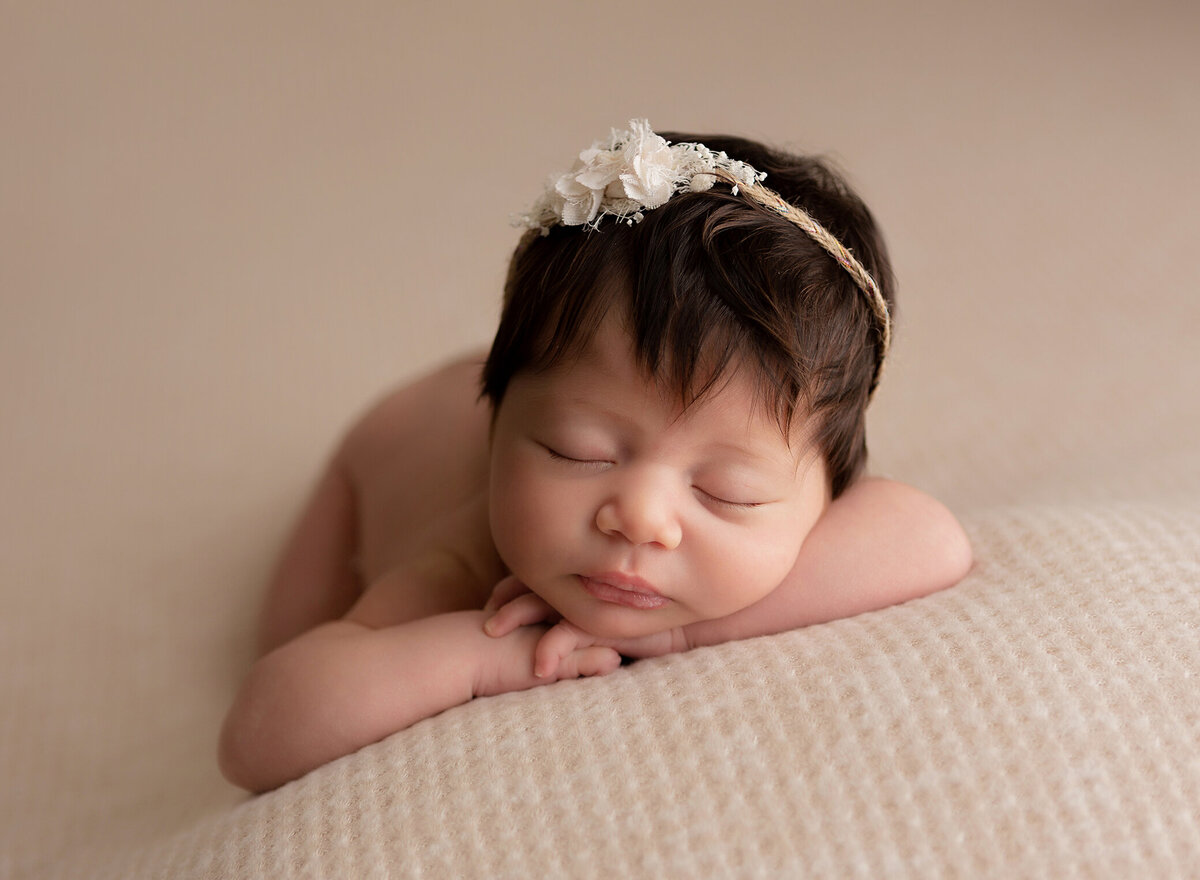 Newborn baby girl photograhed in Irvine California at her newborn session. She is posed on a textured nneutral backdrop and has a tiny bow in her hair