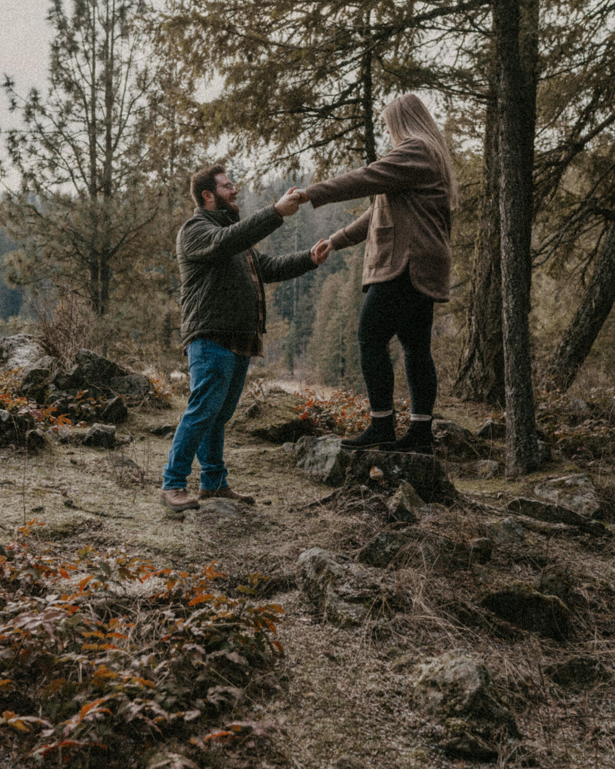 A winter engagement couple laughs and runs through a field during their playful engagement session in Spokane, Washington, highlighting joy and spontaneity.