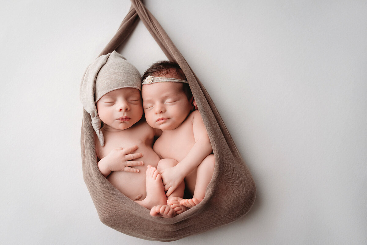 Boy and girl twin newborn babies naked laying together in taupe fabric snuggling each other