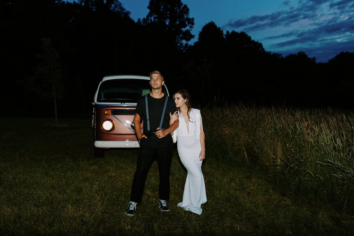 wedding couple with their arms linked and an old style van behind them at night