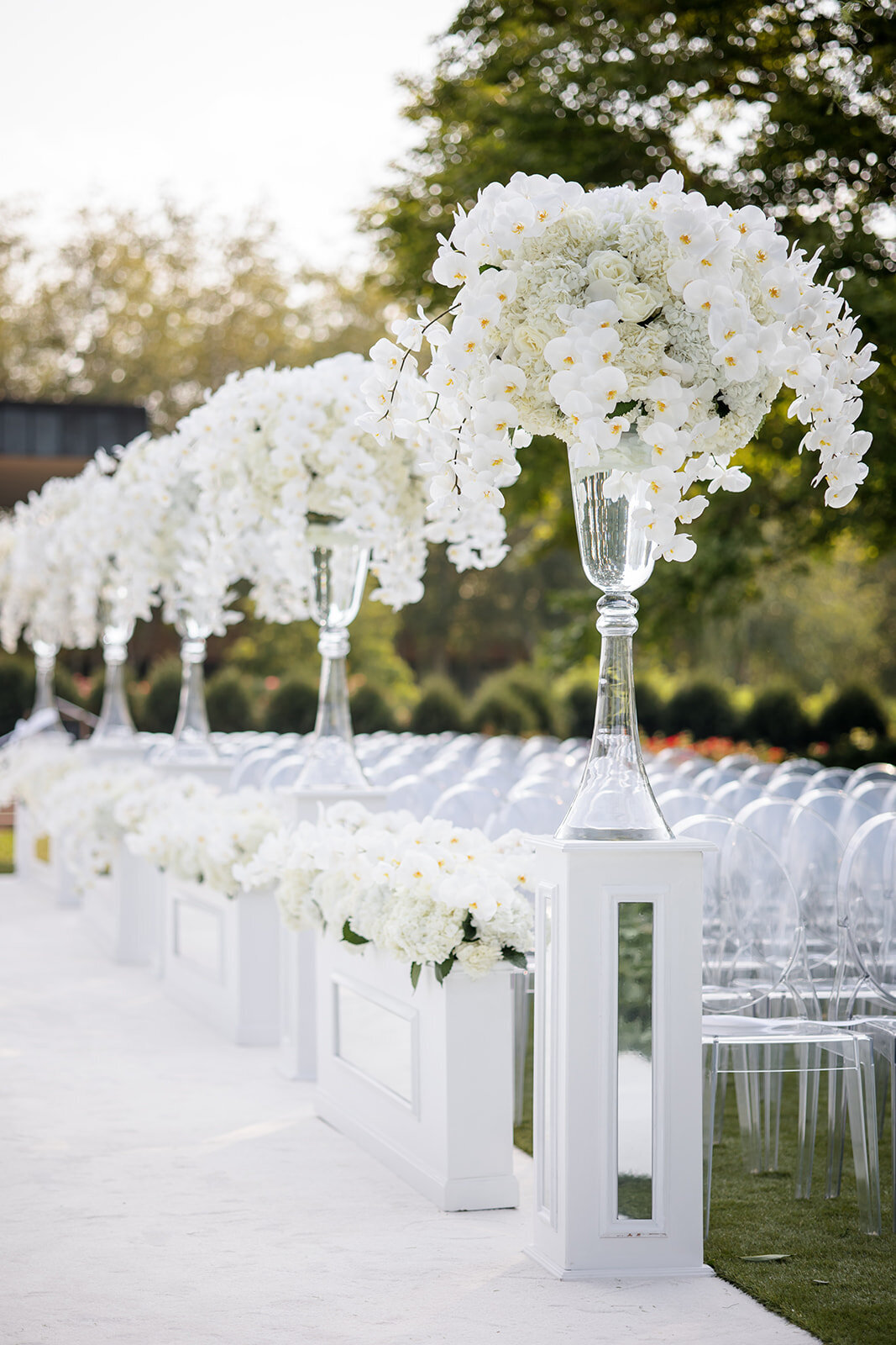 A meticulously decorated wedding aisle at the Chicago Botanic Garden, featuring towering glass vases overflowing with white orchids.