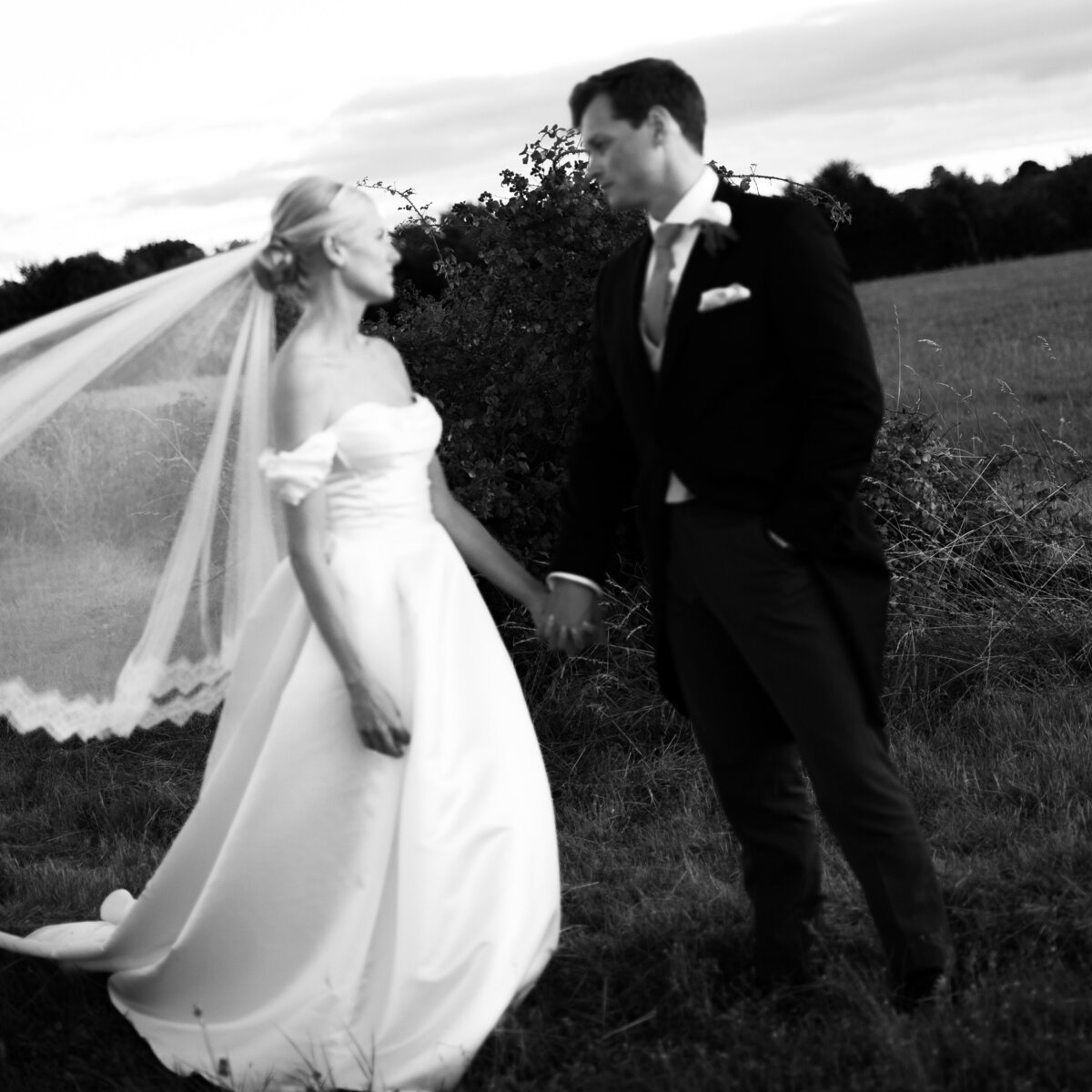 Black and white, slightly out-of-focus in-between moment of a couple’s photo session in a rural English field, captured in a documentary style — by Kate Winters Photography.