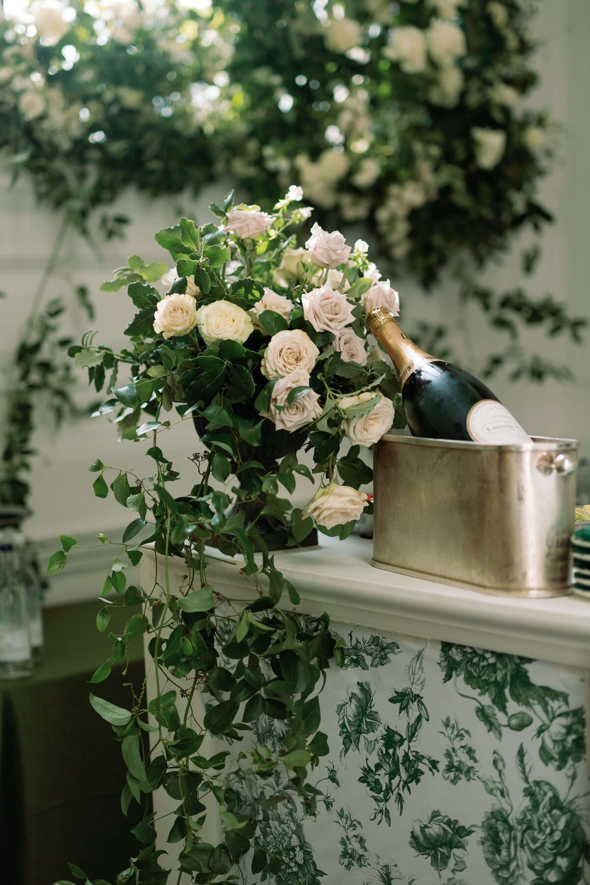 closeup of a green and white floral patterned bar with a bottle of laurent perrier displayed on top of it and surrounded with white roses and green foliage