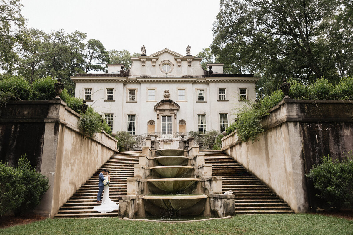 Bride and groom hugging on the stairs in front of the Swan House.