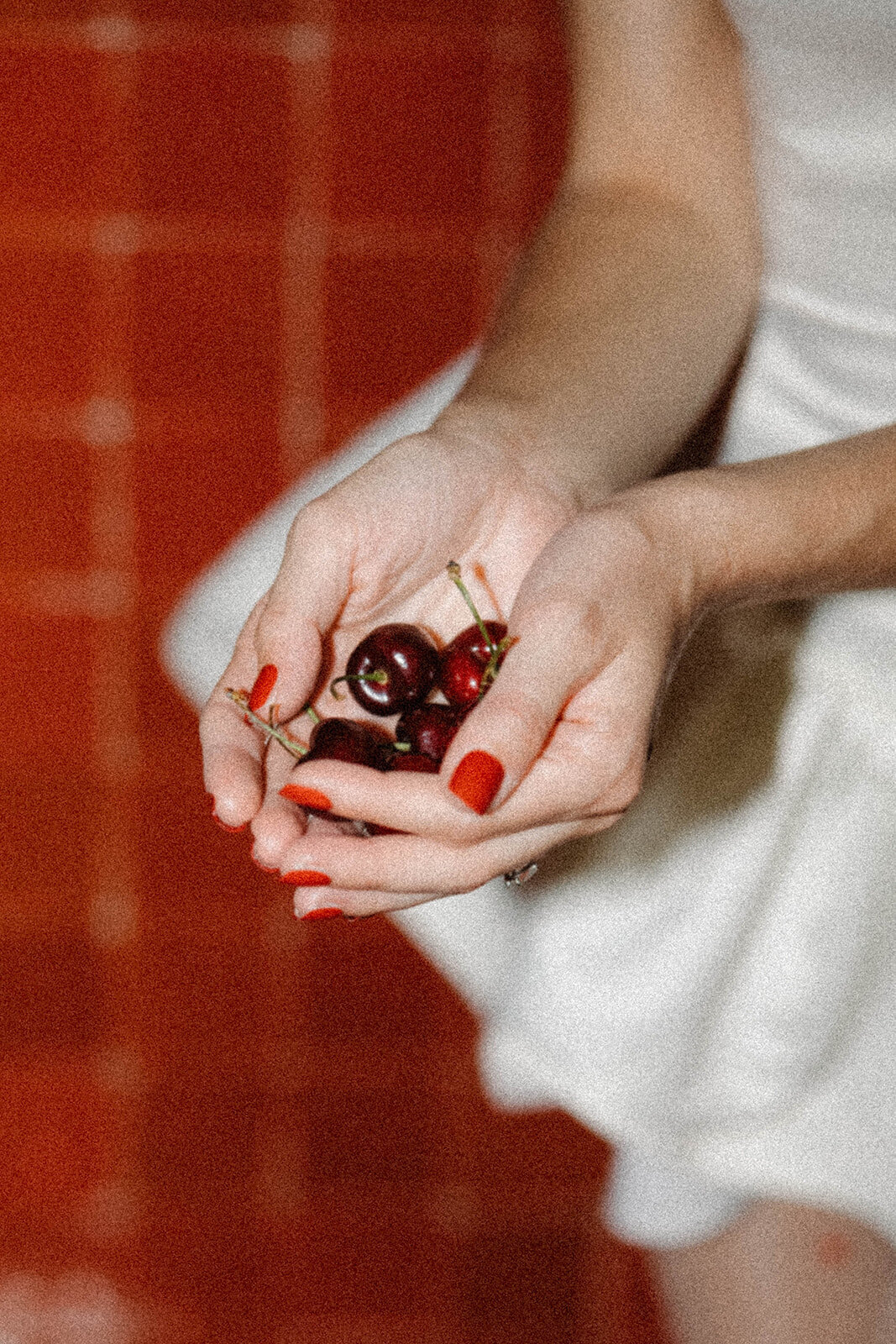 A handful of cherries with red nails and red tiles in the background. 