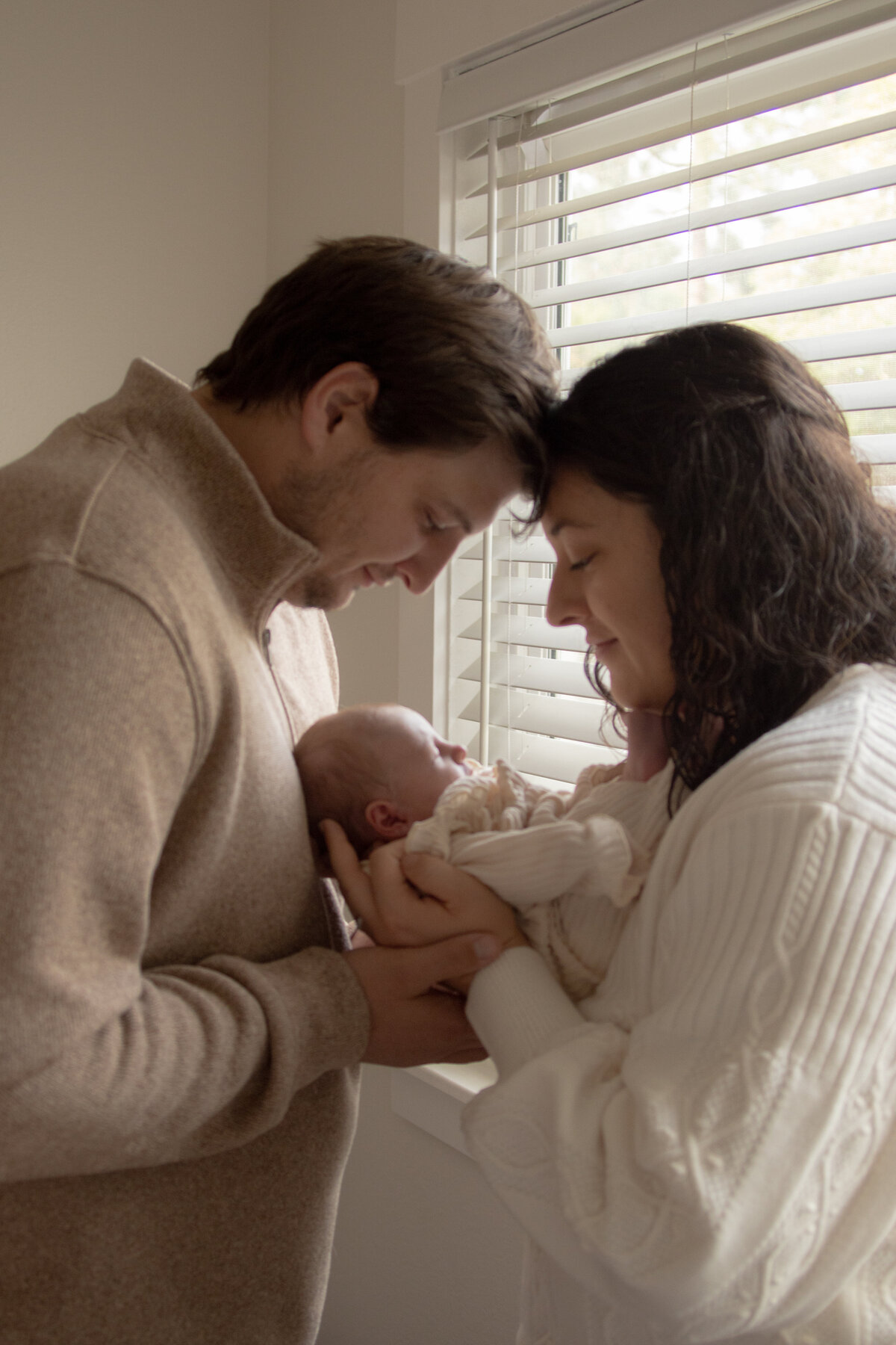 mom and dad admiringly looking down at newborn baby daughter during in-home newborn lifestyle session